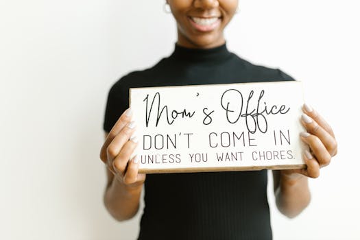 A woman holds a humorous 'Mom's Office' sign, adding a playful touch to home decor.