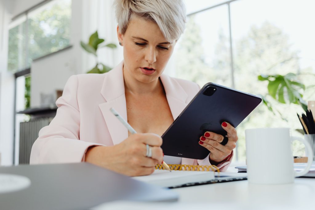 Businesswoman writing notes with tablet in modern office environment.